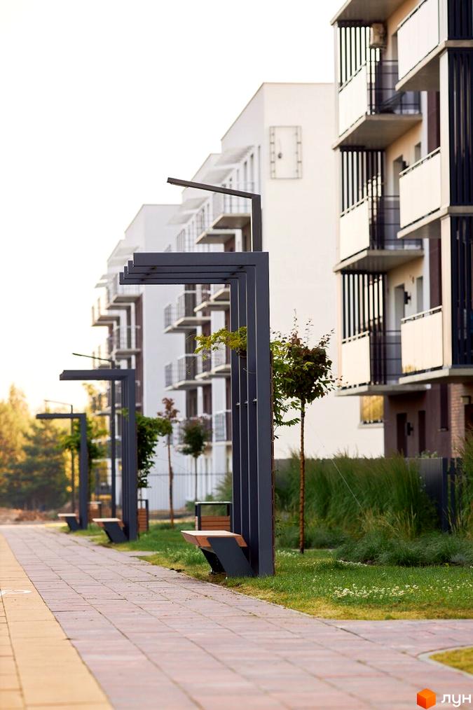 Зображення прибудинкової території Житлового комплексу StyleUP з лавками та освітленням вздовж тротуару. На фоні видно багатоквартирний будинок.