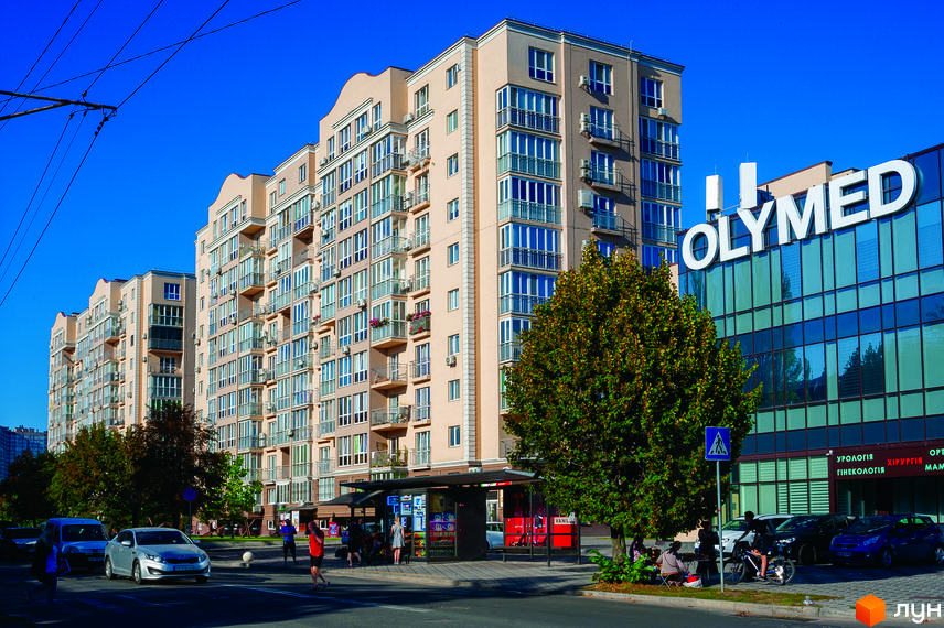 Фасад житлового комплексу ЖК Кришталеві джерела з численними балконами та вікнами. Поруч розташована будівля з вивіскою OLYMED та зелені насадження.