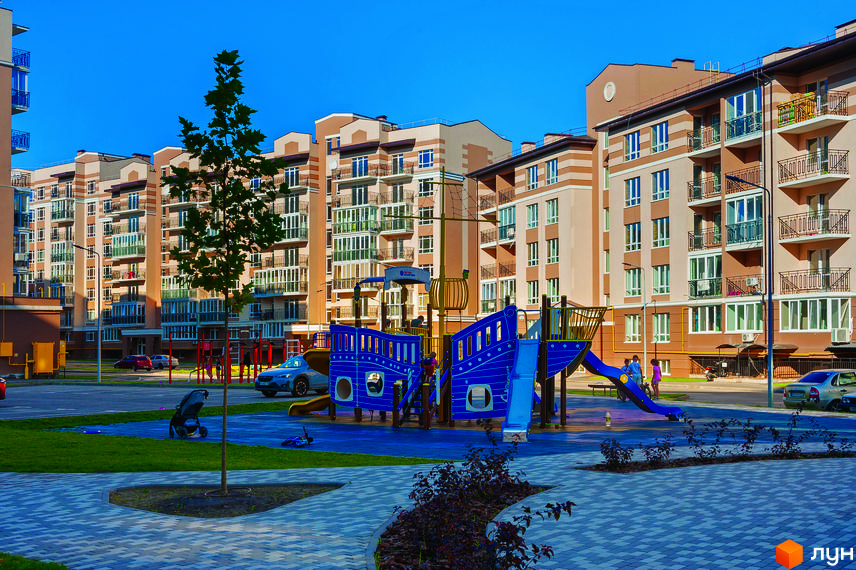 Житловий комплекс Кришталеві джерела: багатоповерхові будинки з балконами та дитячий майданчик у вигляді корабля. Територія комплексу доглянута, з деревами та бруківкою.