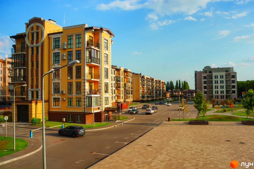 Житловий комплекс Кришталеві джерела. Зовнішній вигляд жовтих та сірих багатоповерхових будинків, парковка з автомобілями та зелена прибудинкова територія з дитячим майданчиком.