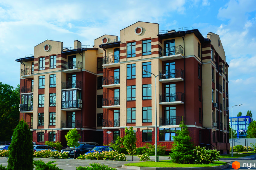 Житловий комплекс Кришталеві джерела. Багатоквартирний будинок з коричнево-бежевим фасадом, балконами та великими вікнами. Навколо будинку зелені насадження та припарковані автомобілі.