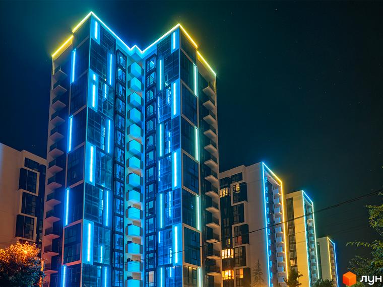Житловий район Manhattan: сучасна новобудова з яскравою неоновою підсвіткою вночі. Будинок має скляний фасад та балкони, виділяється синім та жовтим освітленням.