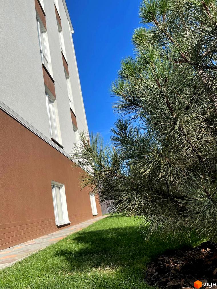 Зовнішній вигляд будинку ЖК SMART IDEA з коричневою та білою обробкою, вікнами та зеленою прибудинковою територією з деревами.