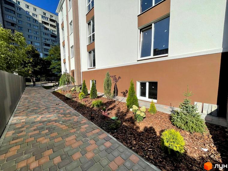 Новобудова ЖК SMART IDEA з коричневим фасадом та цегляними вставками, доглянута прибудинкова територія з бруківкою та зеленими насадженнями.