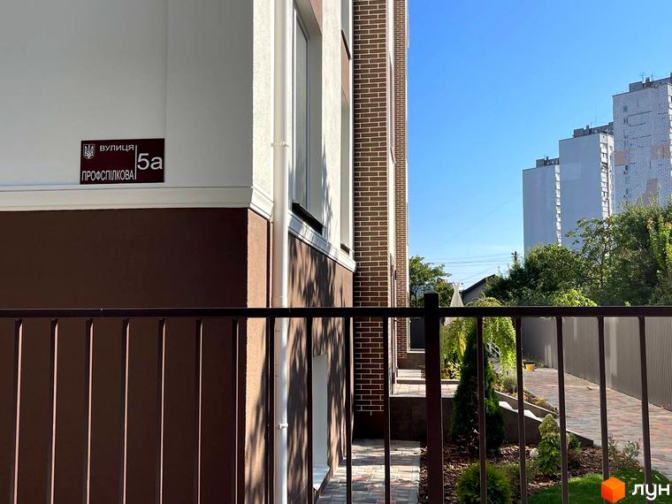 Фасад новобудови ЖК SMART IDEA з табличкою адреси. Прибудинкова територія з огорожею та зеленими насадженнями.