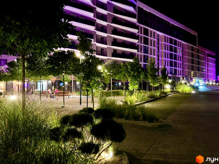 Житловий комплекс Tiffany з фасадами, підсвіченими фіолетовим світлом, та доглянутою прибудинковою територією з деревами та освітленням.