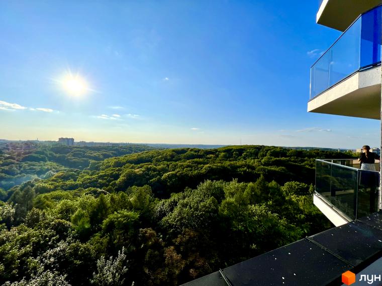 Вид з балкона житлового комплексу Tiffany на зелений ліс та місто. Сучасна архітектура комплексу з панорамним склінням.