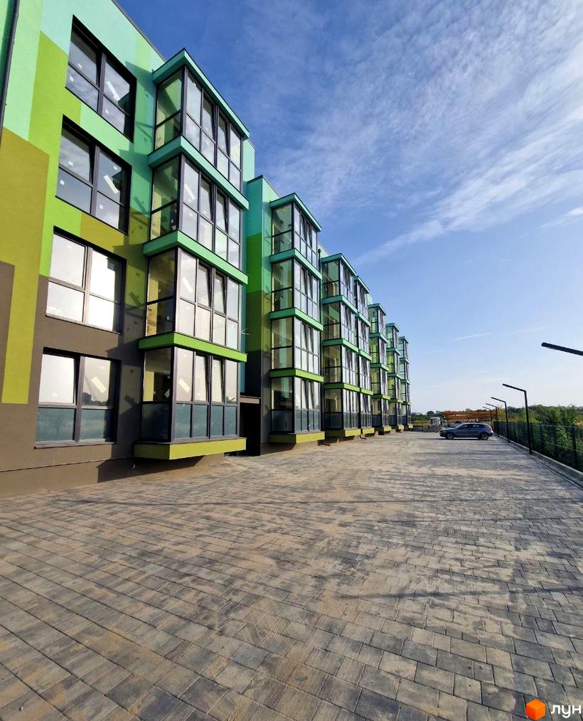 Зовнішній вигляд новобудови ЖК Квітковий з яскравим фасадом та скляними балконами, поруч облаштований паркінг.