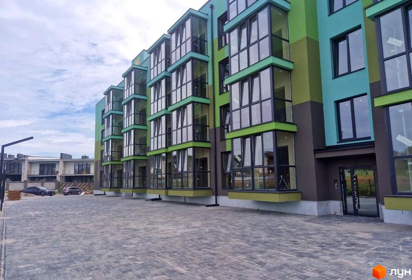 Зовнішній вигляд новобудови ЖК Квітковий з фасадом у бірюзово-зелених тонах та великими панорамними вікнами. Поруч розташований вимощений бруківкою двір.