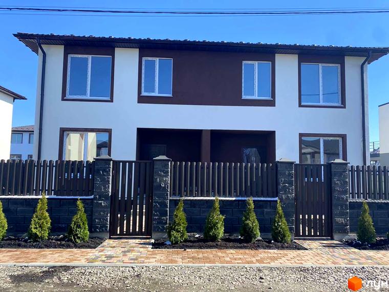 Котеджне містечко КМ Житомирський дворик - 2. Фасад двоповерхового будинку з коричнево-білими стінами та парканом з дерев'яними рейками та кам'яними стовпами.