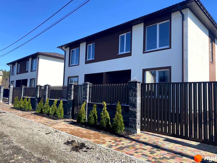 Котеджне містечко Житомирський дворик - 2. Фасад будинку білого та коричневого кольору з великими вікнами. Огороджена територія з доглянутими туями та бруківкою.