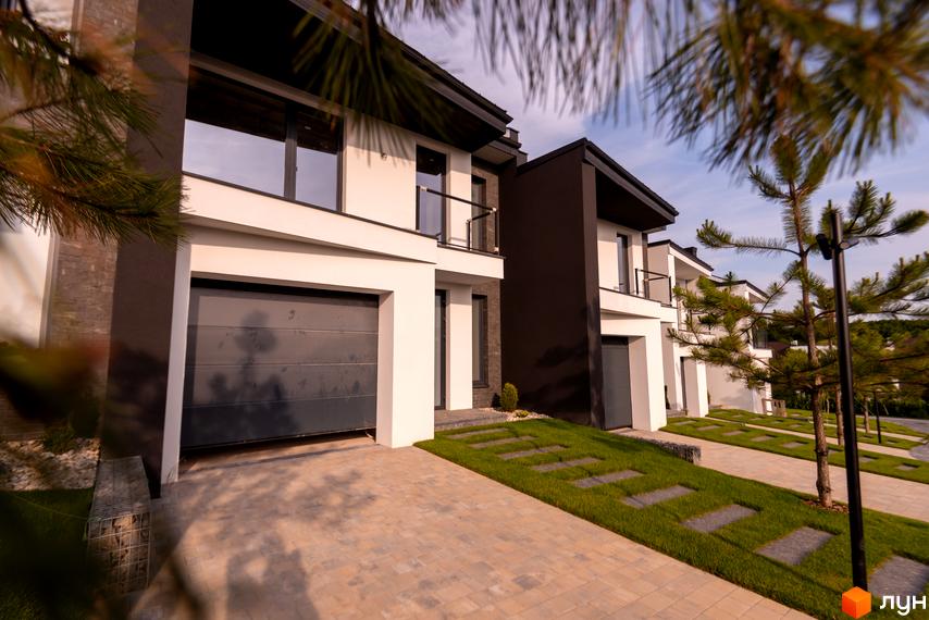 Котеджне містечко КМ SHERWOOD. Зовнішній вигляд будинків з гаражами та балконами, доріжки з плитки та зелені газони.