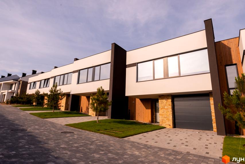 Котеджне містечко КМ SHERWOOD. Зовнішній вигляд будинків з великими вікнами та дерев'яними елементами. Прибудинкова територія з бруківкою та газоном.