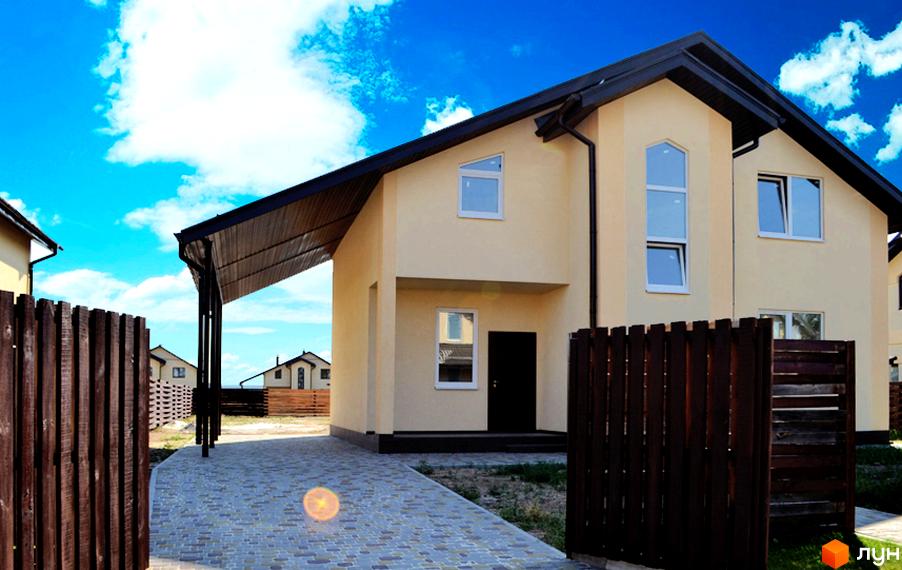 Котеджне містечко КМ Наше містечко. Зовнішній вигляд двоповерхового будинку з навісом та дерев'яним парканом. Навколо будинку облаштована бруківка та зелена зона.