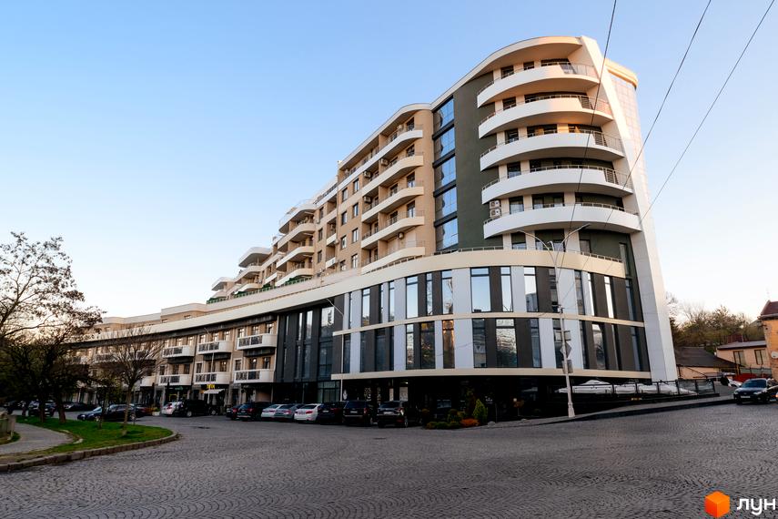 Житловий комплекс DREAM CITY з вигнутим фасадом та балконами. Парковка та зелена зона біля будинку.