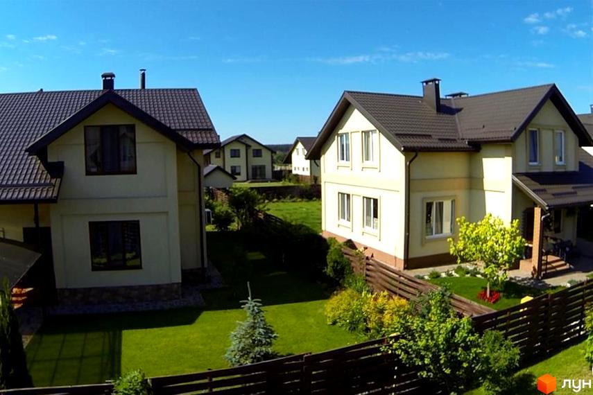 Зовнішній вигляд будинків у житловому комплексі КМ Наше містечко з зеленими прибудинковими територіями та огорожами.