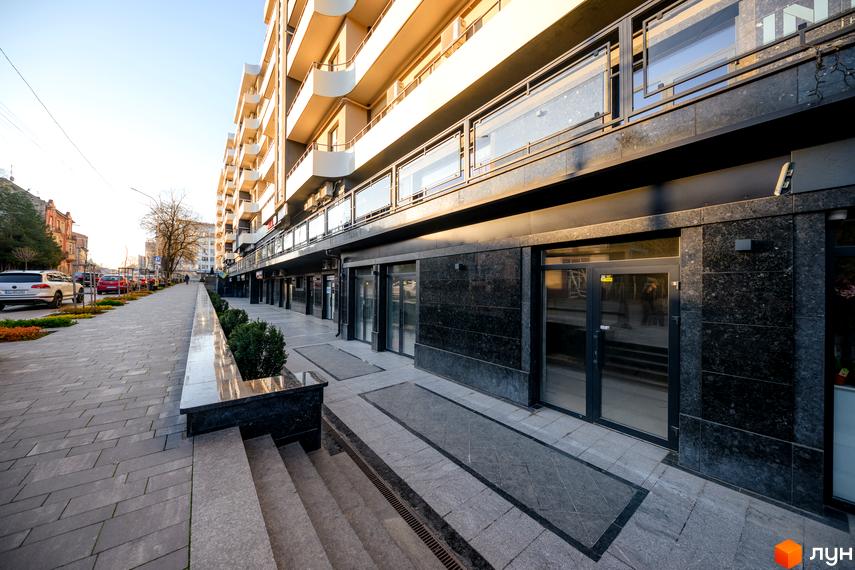 Зовнішній вигляд новобудови ЖК DREAM CITY з фасадом з темного мармуру та балконами. Поруч розташована бруківка та зелені насадження.