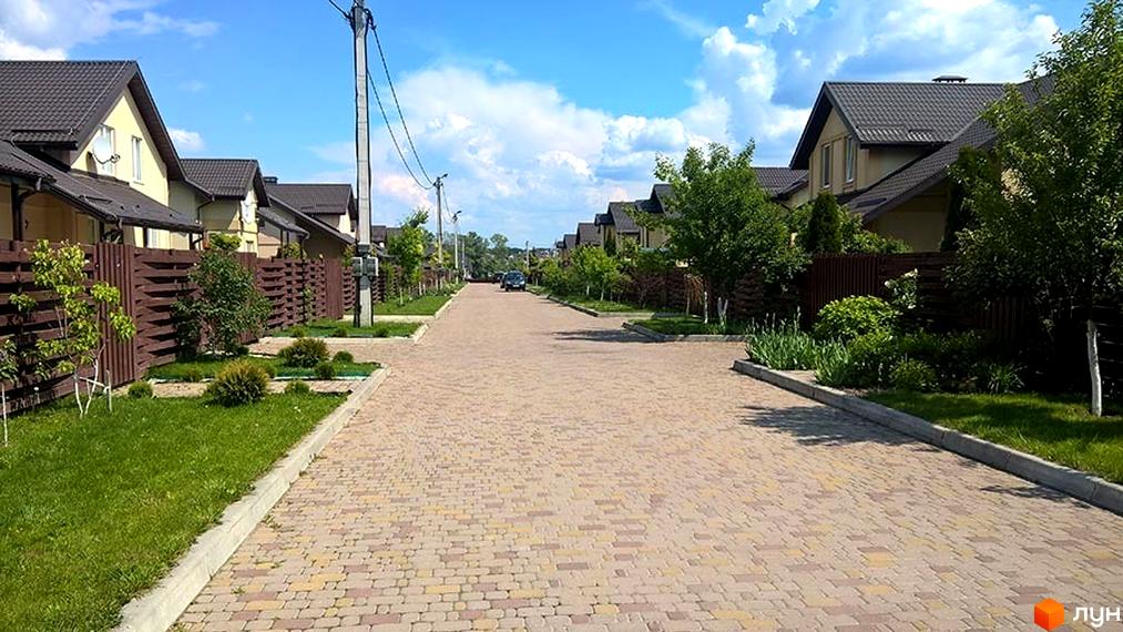 Зовнішній вигляд котеджного містечка КМ Наше містечко з брукованою дорогою та зеленими насадженнями.