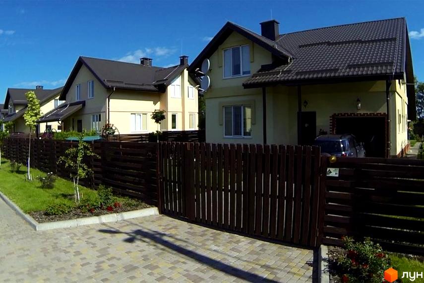 Котеджне містечко Наше містечко. Двоповерхові будинки світло-жовтого кольору з темними дахами та коричневим дерев'яним парканом. Прибудинкова територія з газоном та деревами.