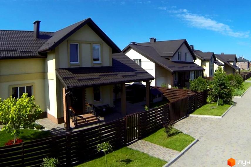 Котеджне містечко КМ Наше містечко: двоповерхові будинки з коричневими дахами, зелені газони та дерев'яні паркани. Територія комплексу доглянута, з бруківкою та деревами.