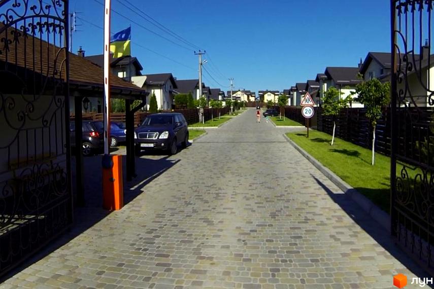 Котеджне містечко Наше містечко. В'їзд на територію котеджного містечка з бруківкою та доглянутими газонами. Сучасні будинки з темними дахами.