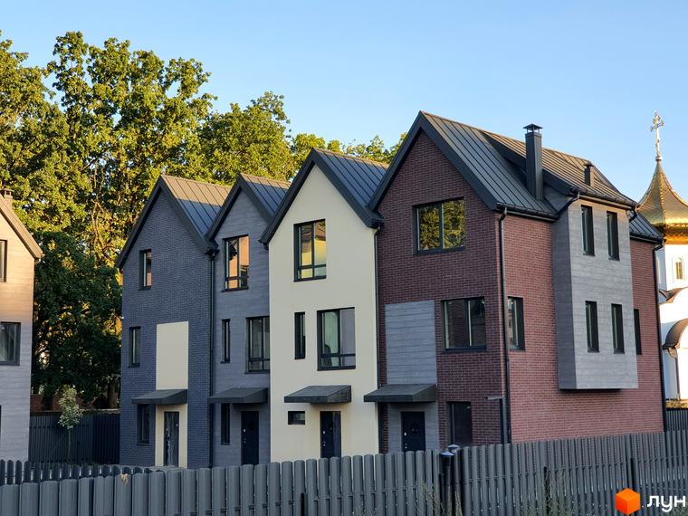 Таунхауси New Smart 11 – це сучасні будинки з цегляним фасадом та сірим дахом, розташовані біля зелених дерев. На території комплексу видно паркан.