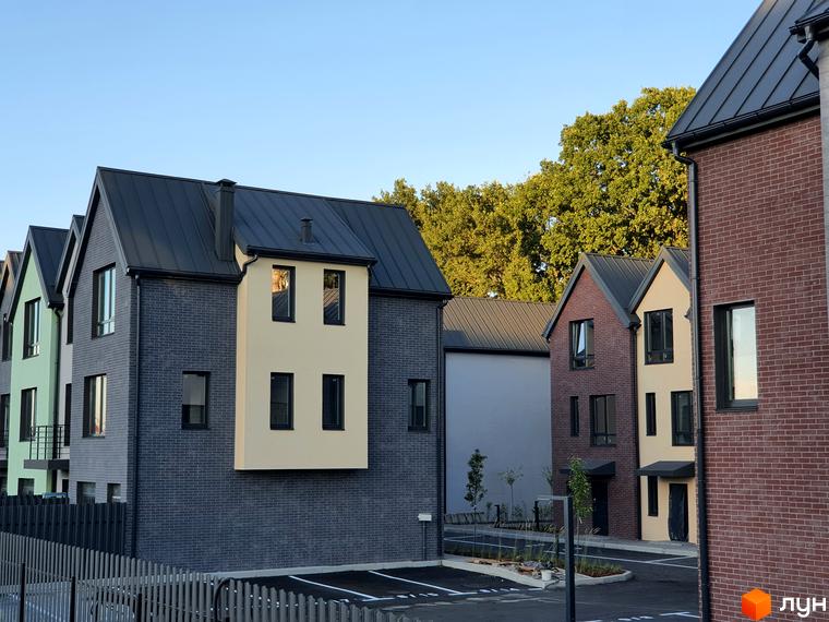 Зовнішній вигляд таунхаусів New Smart 11 з цегляним фасадом та темним дахом. Прибудинкова територія з парковкою та огорожею.