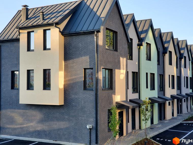 Зовнішній вигляд таунхаусів New Smart 11 з цегляним фасадом та різнокольоровими вставками. Поруч розташована прибудинкова територія з деревами та парковкою.