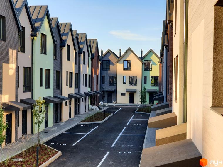 Різнокольорові таунхауси New Smart 11 з сірими дахами та парковкою перед будинками. Зовнішній вигляд новобудови та прибудинкова територія.