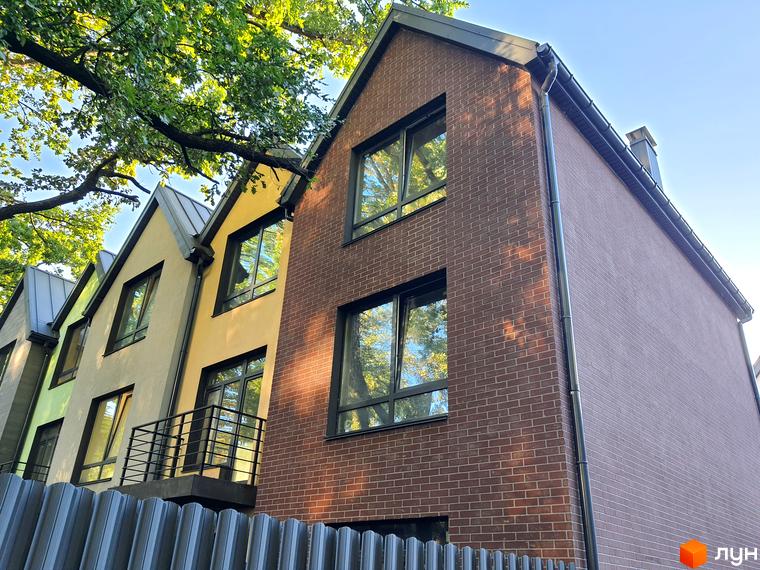 Таунхауси New Smart 11 з цегляним фасадом та жовтими стінами, вікна відображають зелені дерева. Навколо будівель видно зелені дерева та блакитне небо.