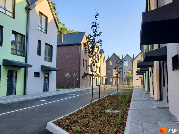 Зовнішній вигляд таунхаусів New Smart 11 з сірими дахами та різнокольоровими фасадами. Прибудинкова територія з бруківкою та зеленими насадженнями.