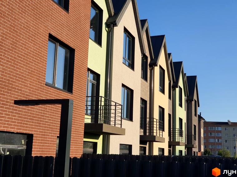 Ряд таунхаусів New Smart 11 з цегляним фасадом та кольоровими стінами під блакитним небом. На передньому плані чорний паркан.