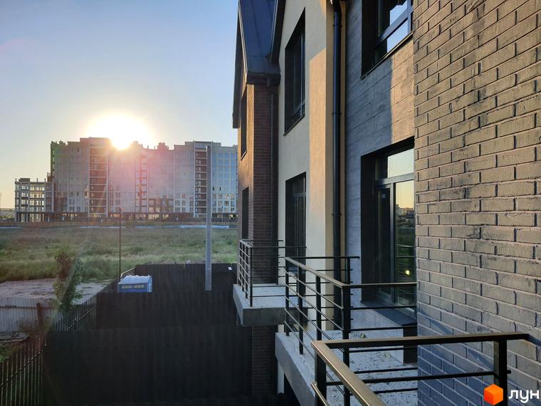 Зовнішній вигляд таунхаусів New Smart 11 з цегляним фасадом та балконами на тлі сонячного неба та багатоповерхових будинків. На прибудинковій території видно паркан та зелень.