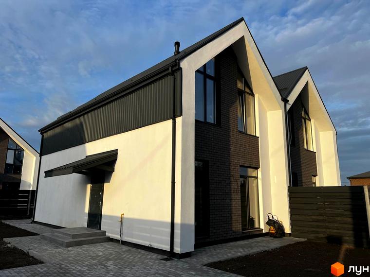 Котеджне містечко КМ New Village. Зовнішній вигляд двоповерхових будинків з білою та темно-сірою обробкою, великими вікнами та чорним дахом. Прибудинкова територія з бруківкою та парканом.