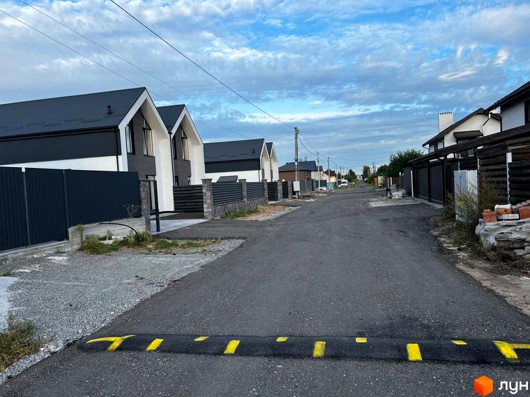 Котеджне містечко КМ New Village: вулиця з сучасними будинками та огорожами. Територія комплексу з асфальтованою дорогою та елементами благоустрою.