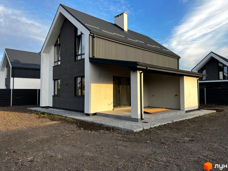 Котеджне містечко КМ New Village: двоповерховий будинок з темним дахом, сірими цегляними стінами та білими елементами фасаду. Прибудинкова територія з бруківкою та зеленими насадженнями.