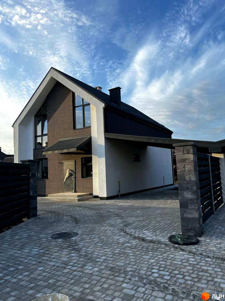 Котеджне містечко КМ New Village: двоповерховий будинок з цегляним фасадом та великими вікнами, прибудинкова територія з бруківки та паркану.