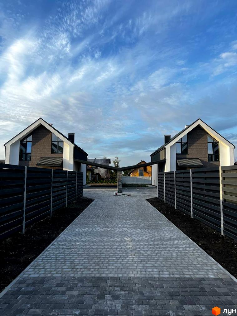 Котеджне містечко КМ New Village: два двоповерхові будинки з темною черепицею та великими вікнами, розділені бруківкою та парканом.