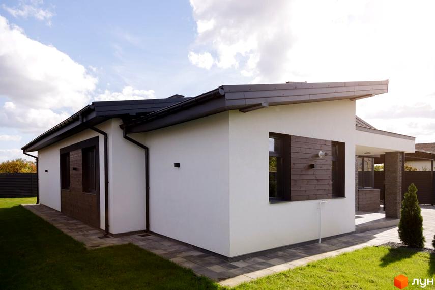 Котеджне містечко КМ New Village: білий одноповерховий будинок з темним дахом та дерев'яними елементами фасаду, зелена галявина та бруківка навколо.