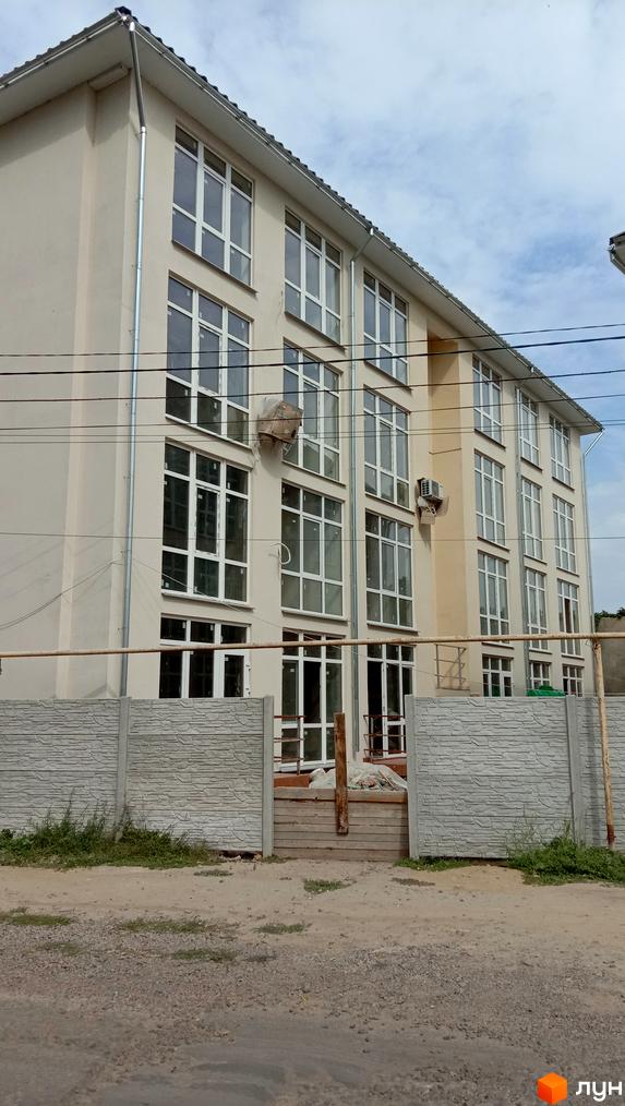 Зовнішній вигляд новобудови ЖК Першотравневий з великою кількістю вікон та сірим парканом. Навколо будинку видно елементи благоустрою території.