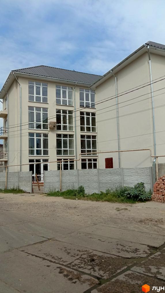 Житловий комплекс Першотравневий - це багатоповерхова новобудова з великою кількістю вікон, розташована біля бетонної огорожі та дороги.