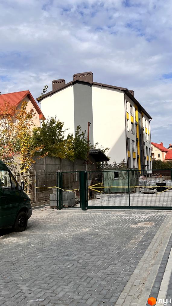 Зовнішній вигляд будинку на вулиці Хіміків. На передньому плані видно прибудинкову територію з тротуарною плиткою та огорожею.