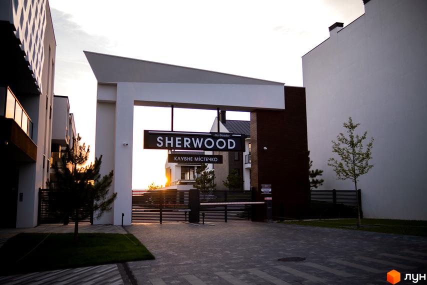 Вхідна група Sherwood КЛУБНЕ МІСТЕЧКО з білими та темними фасадами. Територія перед комплексом вимощена бруківкою, є зелені насадження.