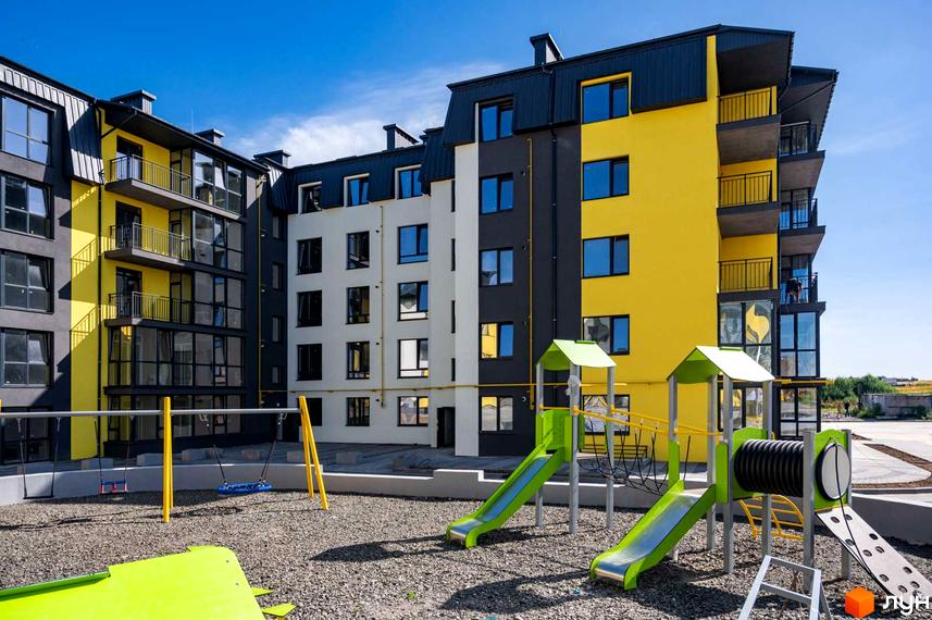 Житловий комплекс Італійський з яскравим жовто-сірим фасадом та дитячим майданчиком з гірками та гойдалками.