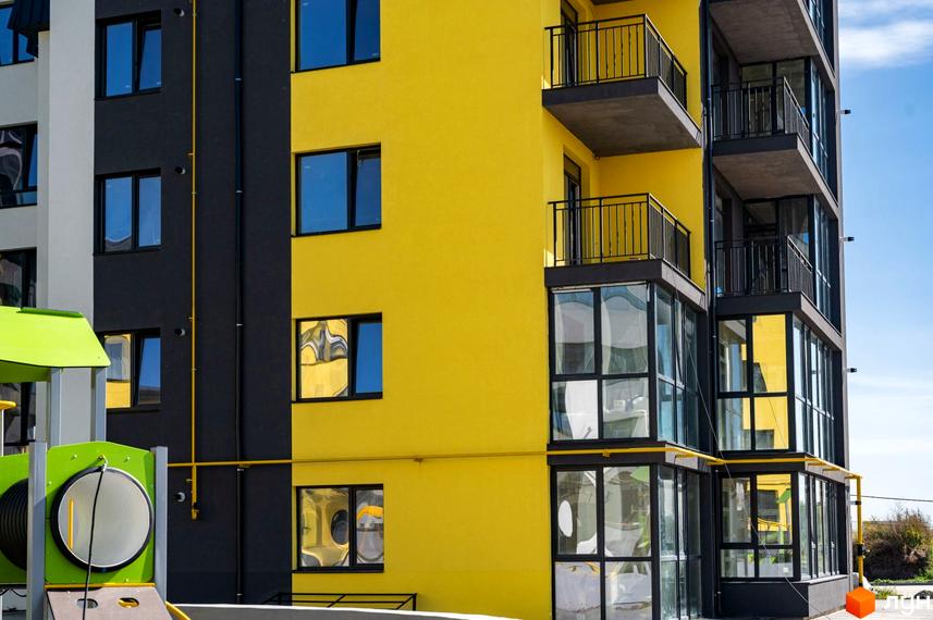 Будинок ЖК Італійський з яскравим жовтим фасадом та чорними елементами. На фото також видно вікна, балкони та частину дитячого майданчика.