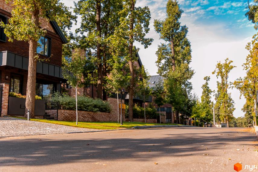 Зображення житлового комплексу Oak Grove Town. Цегляні будинки з великими вікнами та зеленими насадженнями вздовж дороги.