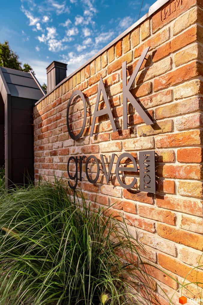 Цегляна стіна з написом Oak Grove Town. Поруч зелені рослини та блакитне небо.