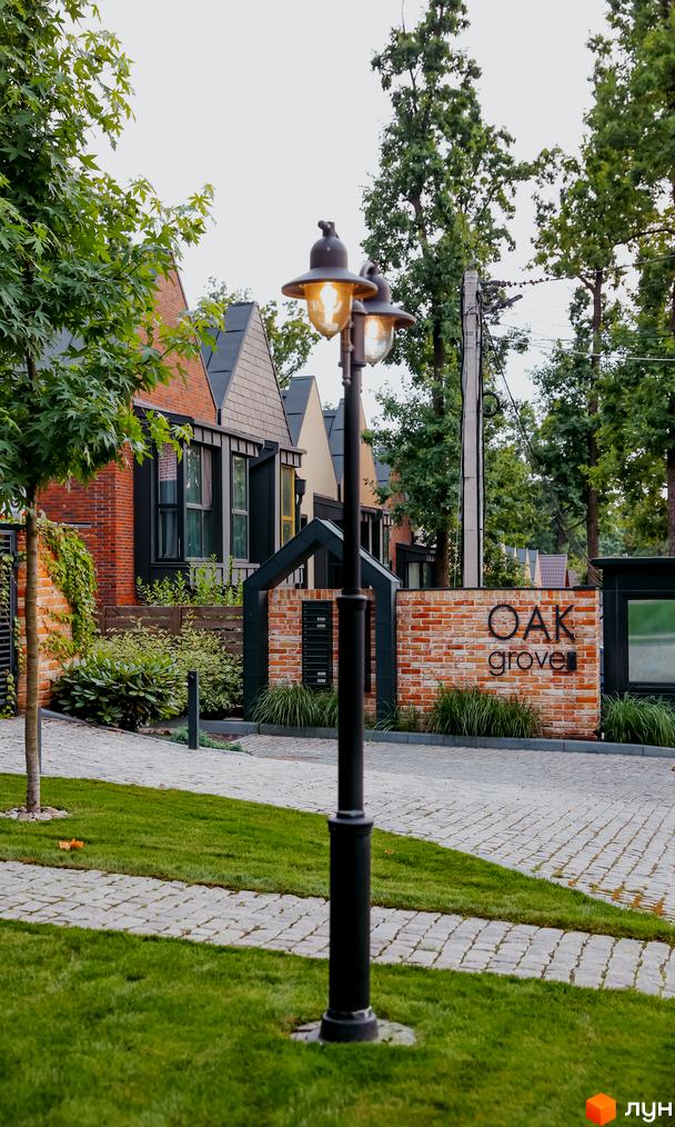 Фасади таунхаусів Котеджного містечка Oak Grove Town з цегли та темними вікнами. Перед будинками зелений газон, бруківка та вуличний ліхтар.