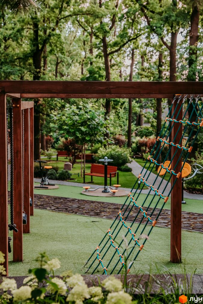 Дитячий майданчик та спортивна зона з дерев'яними елементами та зеленим покриттям на території Котеджного містечка Oak Grove Town.