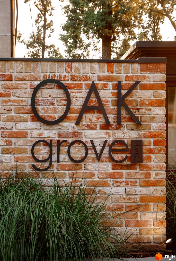 Зображення цегляної стіни з написом Oak Grove Town, що представляє Котеджне містечко Oak Grove Town. Перед стіною розташовані зелені насадження.